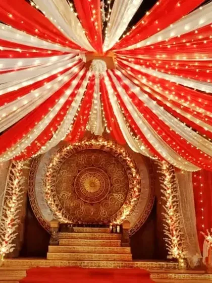 Here is a traditional stage I designed, perfect for a wedding reception or cultural festival. The design features extensive red and white fabric draping across the ceiling, intricate lighting, and a detailed golden centerpiece to create a rich, celebratory atmosphere.