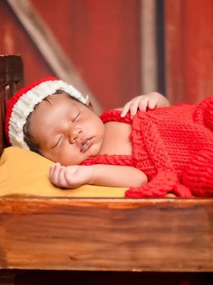 The vibrant red of the Santa outfit and hat stands out beautifully against the rustic wooden props, creating a striking and festive newborn photograph.
