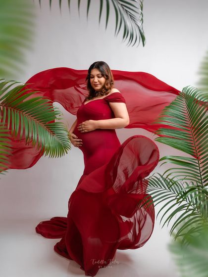 A dance of fabric and foliage. The flowing red gown contrasts beautifully with the sharp green of the tropical leaves, creating a dynamic and visually stunning composition.