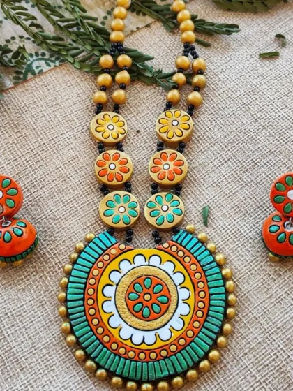 This unique necklace features a round, mandala-style pendant and a chain of smaller floral beads. This version is in a refreshing green, orange, and yellow combination.