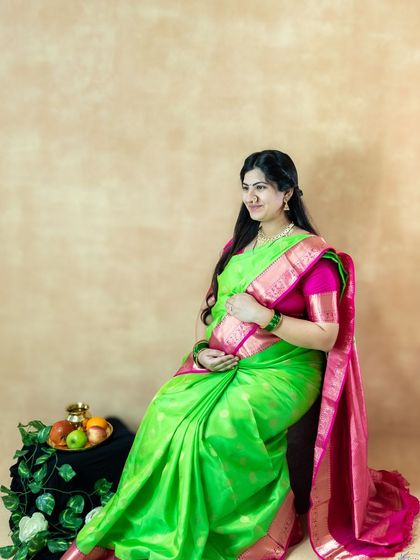 A classic seated portrait of a mom-to-be in a traditional green and pink saree in our studio.