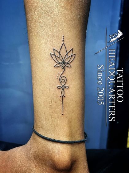 A fine-line Unalome and lotus tattoo on the ankle, symbolizing the path to spiritual enlightenment and purity.