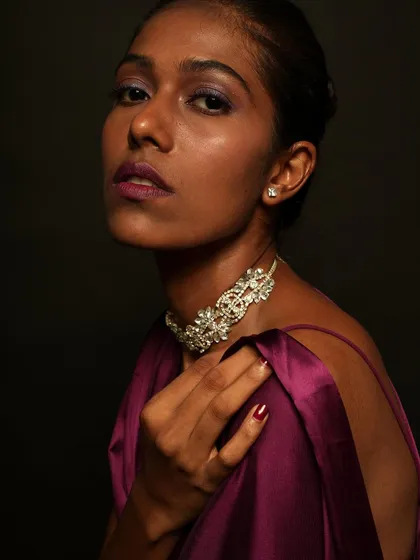 A close up of a model with a purple themed makeup look. I used shades of purple on her eyes and lips to complement her dark skin tone and the purple satin outfit.