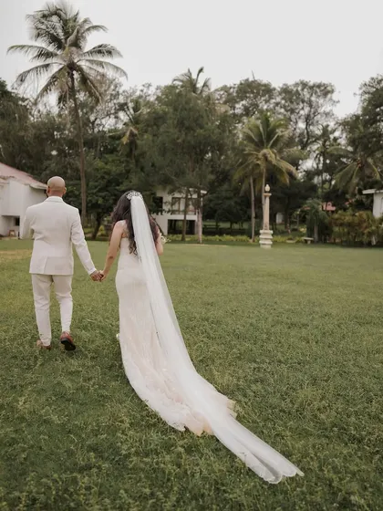 The couple walks away hand-in-hand, the bride's long veil trailing behind her, creating a romantic and cinematic image.