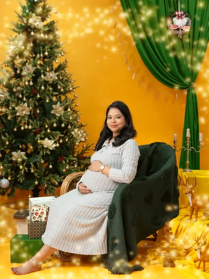 A happy and bright Christmas portrait. The mom-to-be smiles warmly, surrounded by festive lights and presents in this cheerful holiday-themed session.