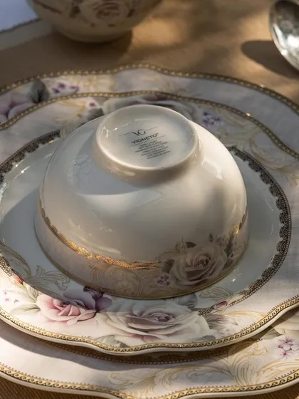 A beautifully lit shot of Vigneto's rose-patterned dinnerware. The sunlight catching the gold rim of the plates highlights the luxurious quality and fine details of the collection.