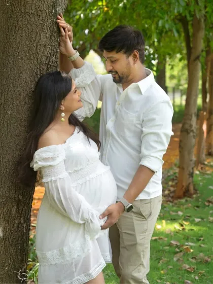A romantic moment shared between the couple, leaning against a tree. The dappled sunlight creates a beautiful, soft effect.