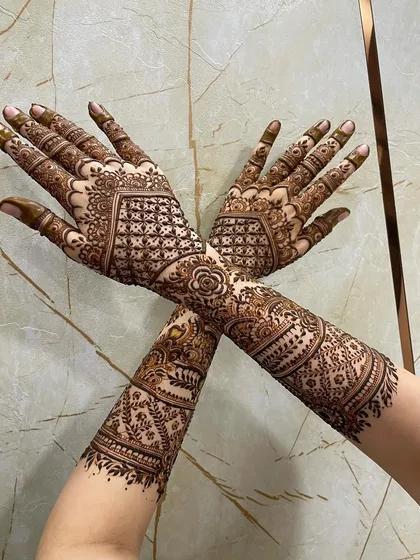 A full bridal mehendi is a statement. This design shows complete coverage from the fingertips to the elbows, featuring a central rose motif connected by detailed gridwork and paisleys for a balanced and striking look.