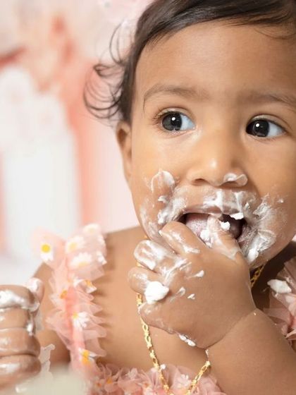 A sweet one-year-old girl enjoying her pink-themed cake smash session. I love capturing these close-ups of their frosting-covered fingers and happy faces.