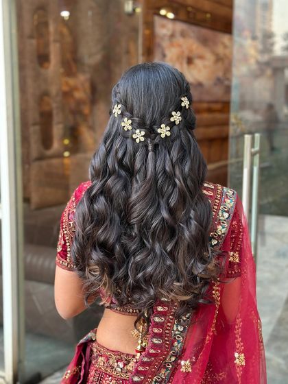 A half-up style with a waterfall braid effect, adorned with small, golden flower clips. The rest of the hair is styled in defined, textured waves.