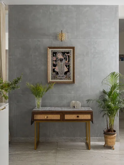 A tranquil corner featuring a traditional Pichwai painting against a modern concrete-finish wall. The simple console table with cane drawers creates a beautiful blend of contemporary design and Indian artistry.