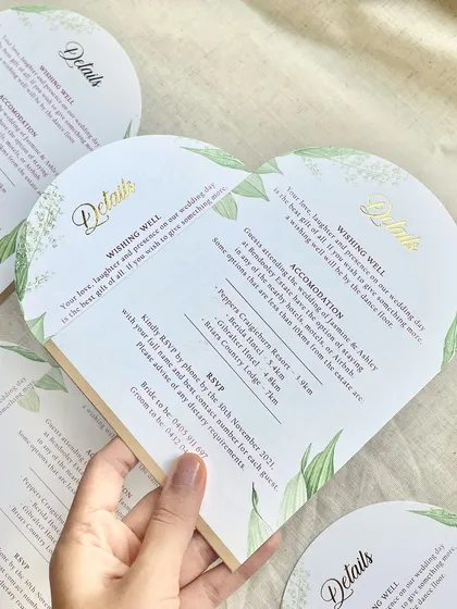 A closer look at a heart-shaped wedding details card. This custom die-cut shape, combined with delicate greenery illustrations and elegant gold foil lettering, adds a touch of romance and whimsy to the invitation suite.