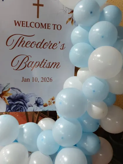 A welcome sign for 'Theodore's Baptism', decorated with a cascade of light blue and white balloons.