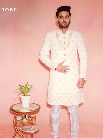 This off-white sherwani features subtle pink embroidery, making it a great option for coordinating with a bride's pastel lehenga. The look is completed with a classic pearl necklace.