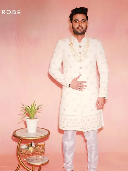 This off-white sherwani features subtle pink embroidery, making it a great option for coordinating with a bride's pastel lehenga. The look is completed with a classic pearl necklace.