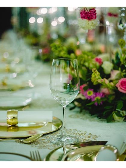 A beautifully focused shot on a wine glass and place setting, with soft floral arrangements in the background. This artistic image captures the delicate balance of elements that contribute to our elegant tablescapes.