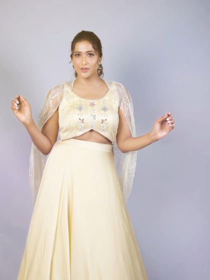 The model showcases the full silhouette of the pastel yellow lehenga. The simple, elegant skirt allows the intricately embroidered blouse and sheer cape to be the focus of this beautiful ensemble.