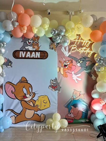 A classic Tom and Jerry theme for a 5th birthday. This setup features a dual backdrop with the iconic characters, a pastel balloon arch, a 'Happy Birthday' neon sign, and a number '5' balloon column.