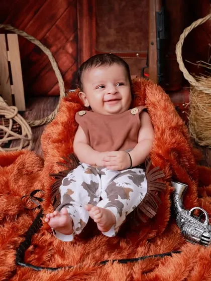 Howdy, partner. This little cowboy smiles brightly in our rustic, western-themed setup, complete with hay, ropes, and a wooden barn backdrop.