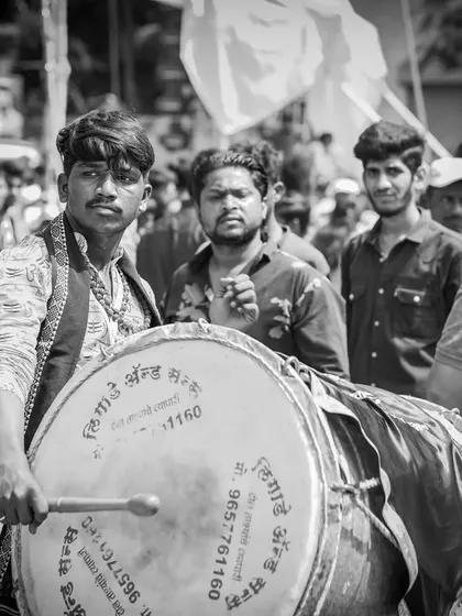 A black and white portrait of a dhol player with an intense look, ready to play.