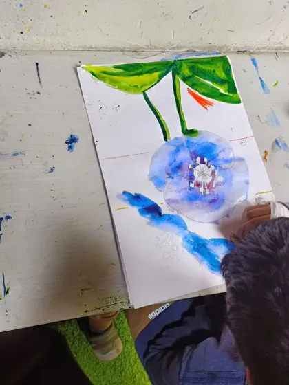 The painting is taking shape. This overhead view shows the progress on the blue flower watercolor, with vibrant greens added for the leaves.