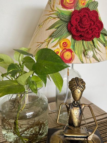 A close-up of a hand-painted and crocheted lampshade, paired with a brass musician sculpture, adding an artistic touch to a corner.
