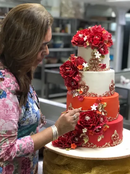 Here I am, adding the final touches to a four-tier mehendi cake. The design features a vibrant red and orange ombre effect, adorned with intricate gold detailing and cascading red sugar peonies to match the festive occasion.