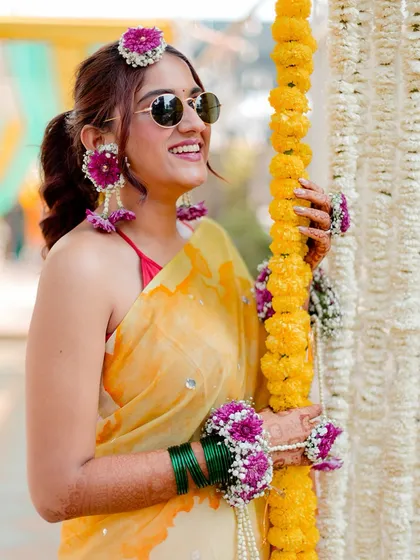 A beautiful, sun-kissed shot of the bride enjoying her Haldi ceremony, with her floral jewelry and bright smile.