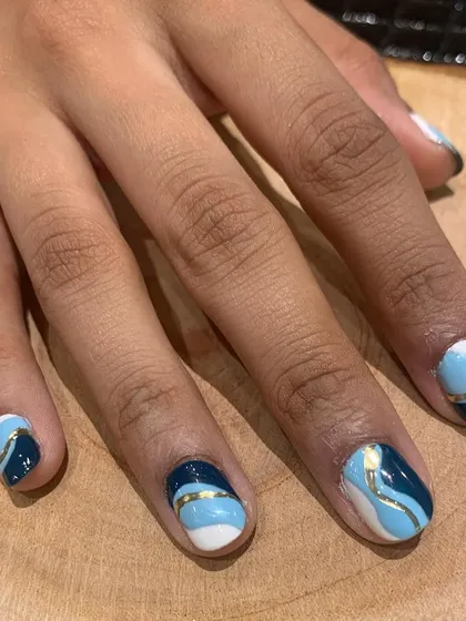 Inspired by the sea. This abstract nail art uses shades of white, light blue, and navy with a gold stripe to create a beautiful wave effect across the nails.