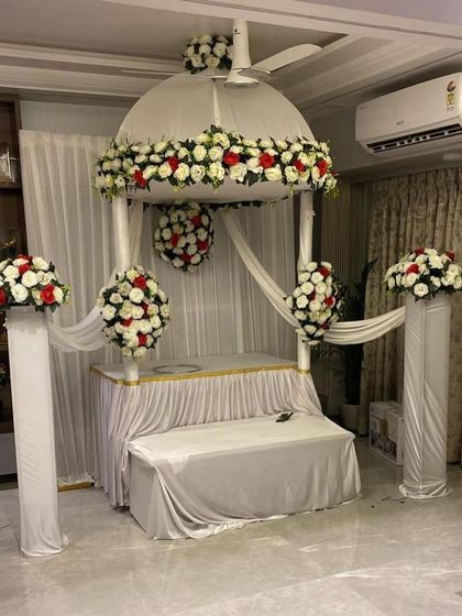 A majestic dome-shaped mandap in white, accented with red and white flower arrangements. The pillars and hanging floral balls add to the structural beauty of this grand design.