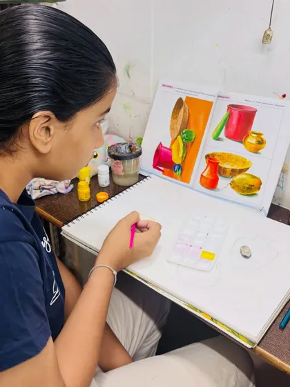 A student carefully studies a reference image to understand the composition and color scheme for her still life painting. We teach students how to deconstruct and replicate complex arrangements.