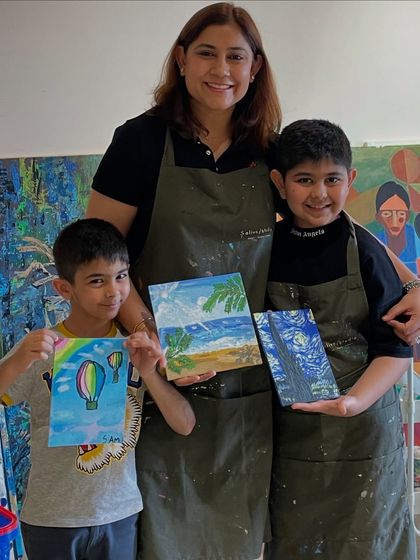 A mother and her two sons proudly show the paintings they created together during a family art session. Our studio is a welcoming space for artists of all ages.