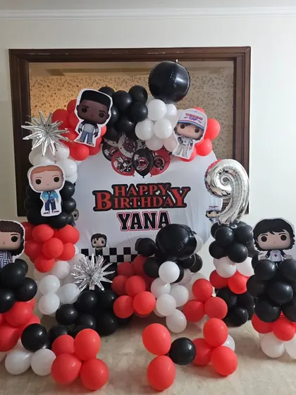 The complete 'Stranger Things' birthday setup for Yana's 9th birthday, featuring a custom backdrop, a silver number '9' foil balloon, and multiple balloon pillars with character cutouts.