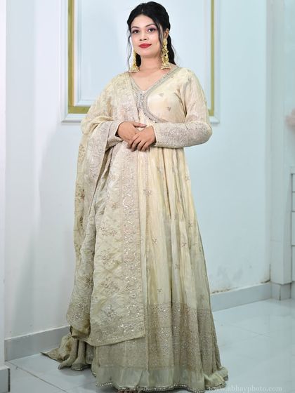 A full-length view of a model in a graceful ivory Anarkali gown with delicate silver embroidery. This is a timeless and elegant option for any wedding guest.