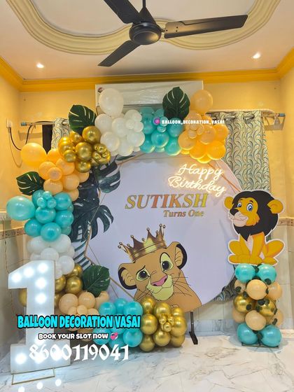 A royal first birthday with a Simba from The Lion King theme. The setup includes a custom backdrop, a marquee number '1', and a balloon arrangement in teal, orange, and gold.