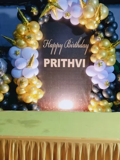 A classic black, white, and gold theme for a milestone birthday celebration. This setup features a custom shimmer backdrop, a balloon arch with star accents, and fun details like a disco ball and a champagne bottle balloon column to get the party started.
