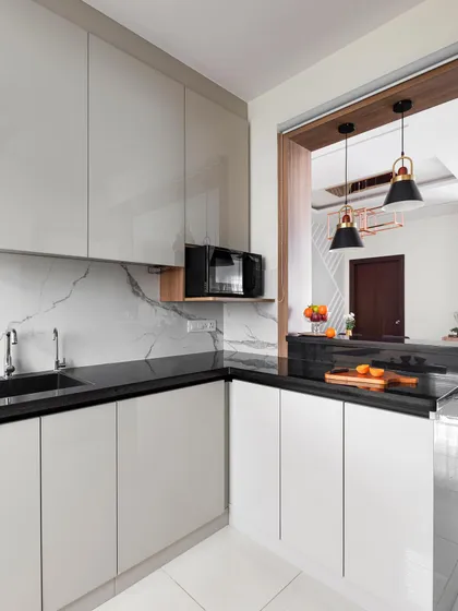 This kitchen features an open pass-through to the dining area, creating a social connection between the two spaces. The design uses light grey acrylic cabinets and a black granite countertop for a classic, high-contrast look.