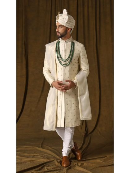 A side view of the 'ARAMBH' sherwani, showcasing the flow of the garment and the consistent, detailed embroidery that makes it a timeless piece for any groom.