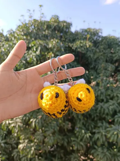 A pair of my smiling bee keychains, held up to the sky. Their cheerful design is always a customer favorite.