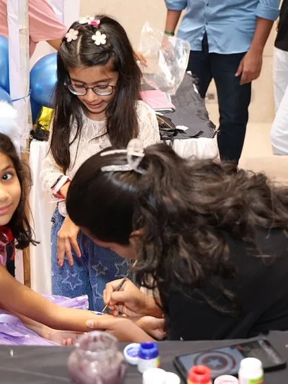 A face painter carefully applies a design to a little girl's arm. This is a classic party activity that I can arrange with talented artists.