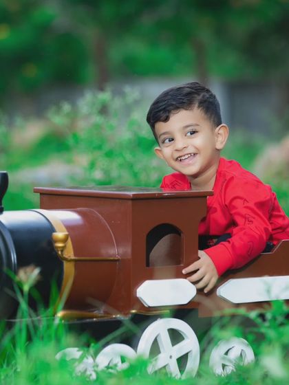 A happy little boy enjoys a ride in a toy train during his fun and playful outdoor photoshoot.