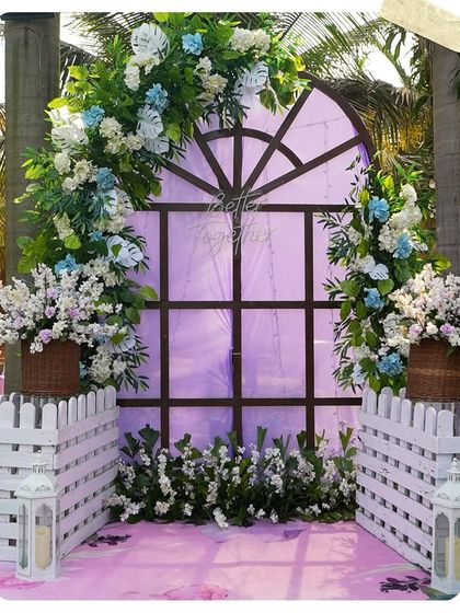 A charming photo booth setup with a window frame, floral arrangements, and a white picket fence. It's a perfect spot for guests to capture memories.
