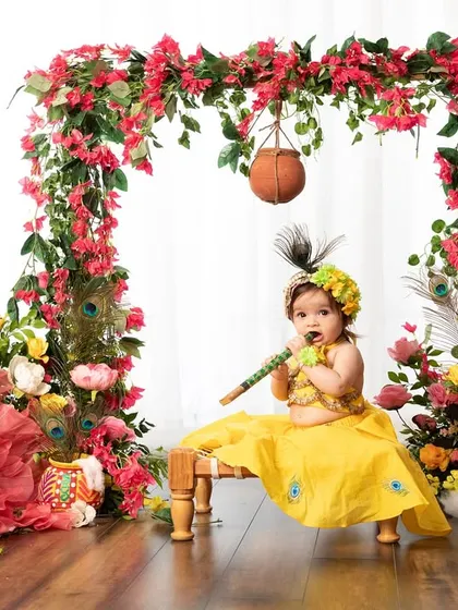 A playful little Radha with her flute, sitting under a beautiful arch of flowers. The hanging matki adds a perfect touch to this Janmashtami scene.
