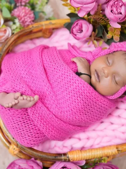 An overhead view of a newborn in a pink knit wrap, sleeping in a basket adorned with matching pink flowers. This composition creates a beautiful, floral-themed portrait.