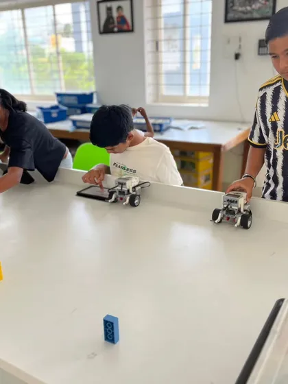 Three students test their robots simultaneously, learning about navigation and sensor interaction in a friendly, competitive setting.