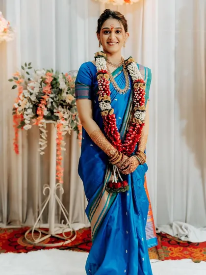 A full-length shot of an engagement bride in a stunning royal blue saree, adorned with a traditional flower garland.