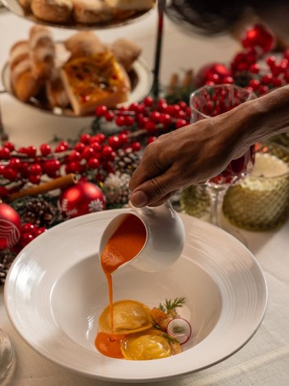 A rich, red sauce being poured over the ravioli, adding another layer of flavor and visual appeal to the dish.