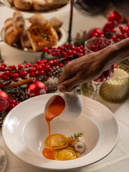 The final touch of pouring a vibrant tomato sauce over our ravioli, an action shot that highlights the interactive plating experience of The Dinner Box.