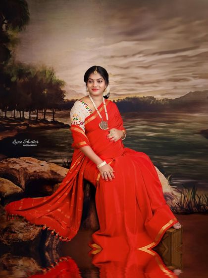 The reflection in the water adds a beautiful, artistic element to this traditional saree portrait, doubling the impact of the rich red color.