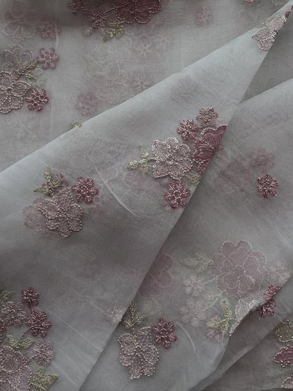This organza fabric showcases a dense cluster of floral appliqué in shades of mauve and pink. The layered effect of the embroidery adds a rich texture, ideal for the yoke of a kurta or an all-over blouse design.